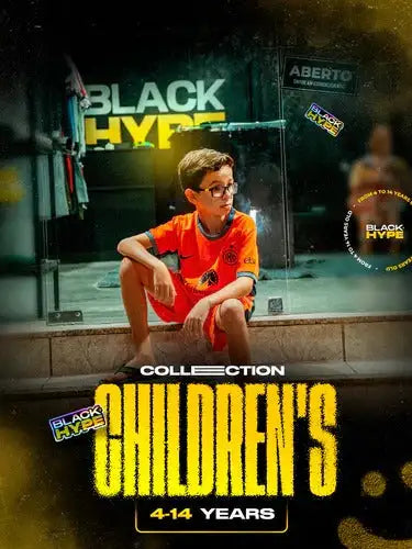 A young boy wearing an orange short-sleeved shirt with a black logo sits on the ground in front of a glass storefront.